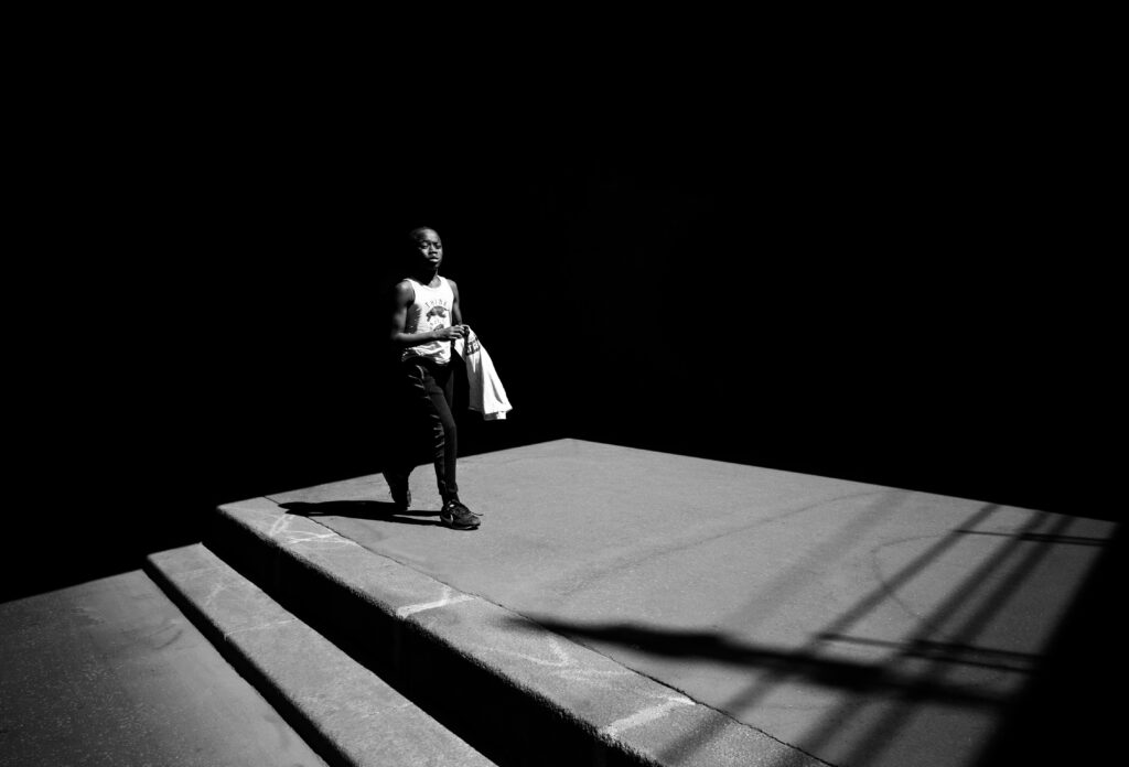 A man walking on a shadowy platform in a high contrast black and white scene.